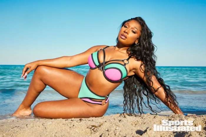 Megan Thee Stallion sits on the sand in a pink and green underwire bikini set.